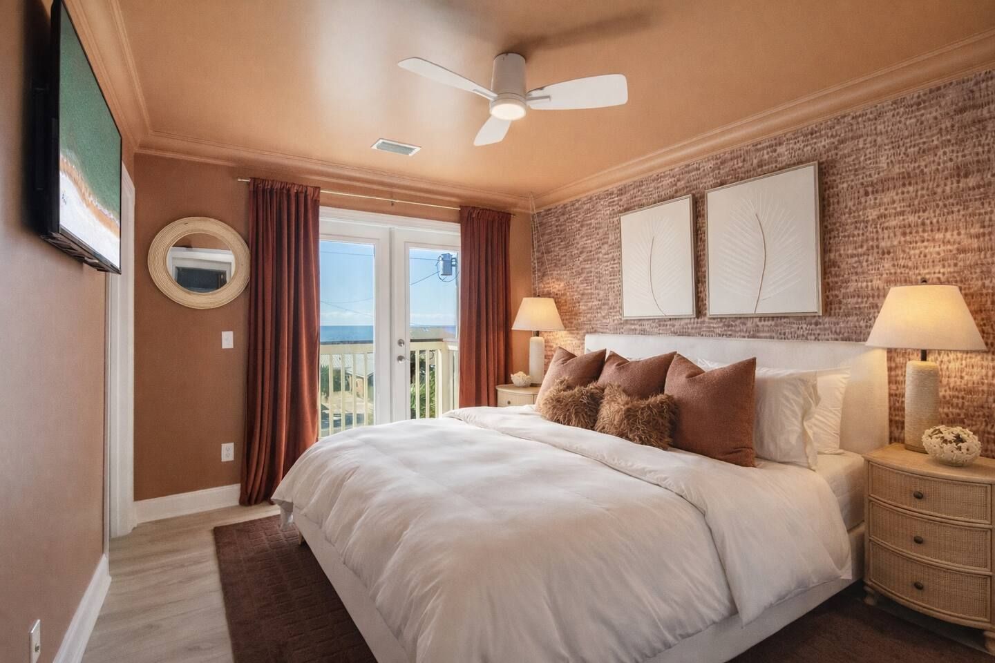 Een slaapkamer met een groot bed, twee bedlampen, een plafondventilator en uitzicht door een glazen deur.