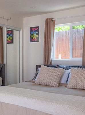 A bedroom with a bed, a window with curtains, a door, and a wall with a poster. - Private Casita in Lake Balboa w/ Gate & Backyard (Los Angeles)