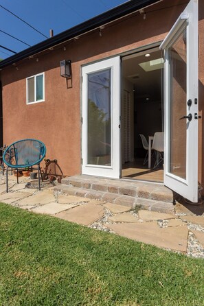 A house with a sliding glass door entrance, a patio with a chair and potted plants, and a small window above the door. - NEW Private Casita in Lake Balboa with Gate & Backyard (Los Angeles)