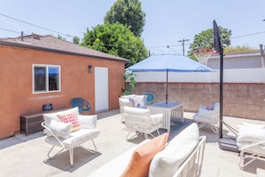 An outdoor patio with white furniture, a blue umbrella, and a basketball hoop. - Private Casita in Lake Balboa w/ Gate & Backyard (Los Angeles)