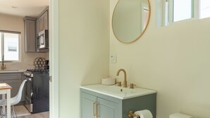 Un baño con inodoro, lavabo y espejo. Hay una ventana sobre el espejo.