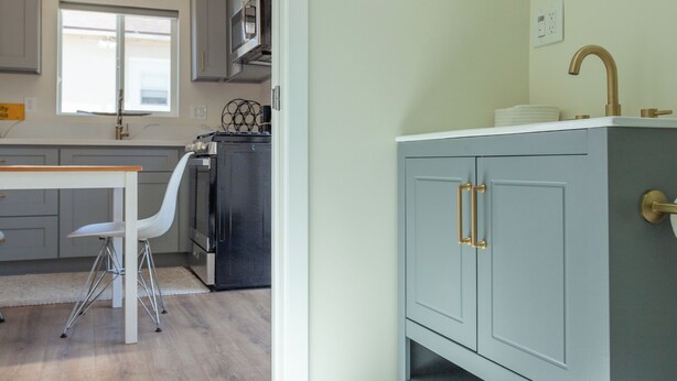 Un baño moderno con tocador gris, espejo redondo y lavamanos blanco.