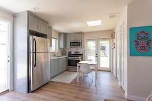 A modern kitchen with stainless steel appliances, a dining area with a white table and chair, and a view through the glass door. - Private Casita in Lake Balboa w/ Gate & Backyard (Los Angeles)