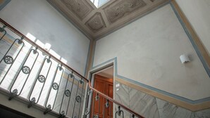 A staircase with a wooden handrail and metal balusters, leading to a room with a wooden door and a ceiling with decorative molding. - House Giotto 33 (Firenze)