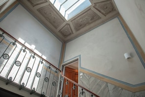 Eine Treppe mit einem hölzernen Geländer und Metallspindeln, die zu einem Raum mit einer Holztür und einer Decke mit dekorativer Stuckleiste führt.