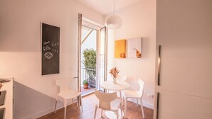 A modern kitchen with white cabinetry, a dining area with white chairs, and a large window with a view of greenery outside. - Vrbo Property (Firenze)