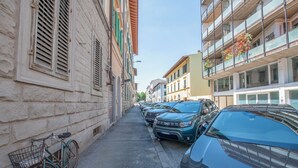 A narrow street lined with parked cars and a bicycle. Buildings on either side have balconies with plants. - House Giotto 33 (Firenze)