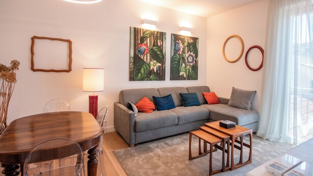 A modern living room with a grey sofa, colorful cushions, a wooden coffee table, and two wall-mounted paintings. - House Giotto 33 (Firenze)