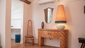 A room with a wooden herringbone-patterned console table, a wicker chair, a mirror, and a lamp with a textured lampshade. - House Giotto 33 (Firenze)