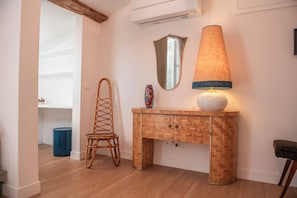 Ein Zimmer mit einem Holzkonsolentisch im Fischgrätmuster, einem Korbstuhl, einem Spiegel und einer Lampe mit strukturierter Lampenschirm.