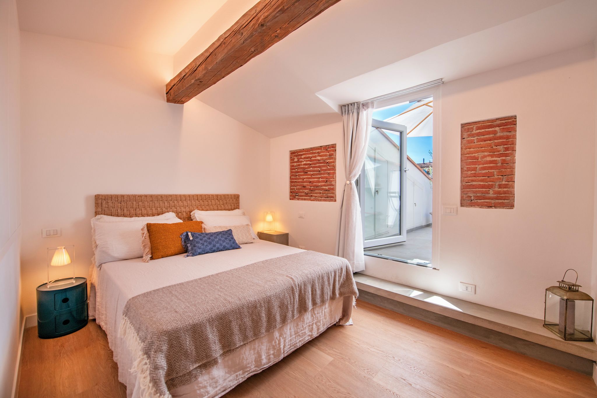 A bedroom with a bed, bedside lamps, a window with curtains, and a brick wall.
