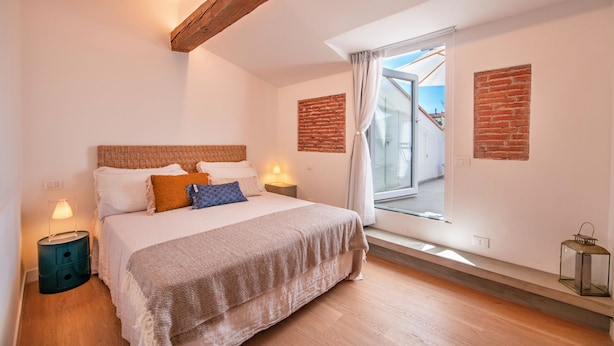 A bedroom with a bed, bedside lamps, a window with curtains, and a brick wall. - Vrbo Property (Firenze)