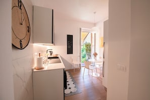 A modern kitchen with a clock, a dining area with a table and chairs, and a view of greenery outside. - House Giotto 33 (Firenze)