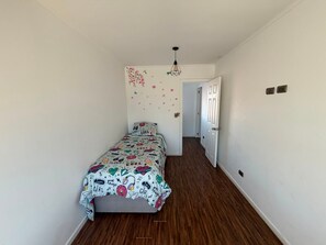 Un dormitorio con una cama individual, una puerta y un pasillo que conduce a otra habitación.