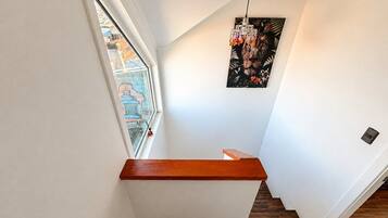 A modern staircase with a wooden handrail, a view of the outside through a window, and a wall-mounted light fixture.