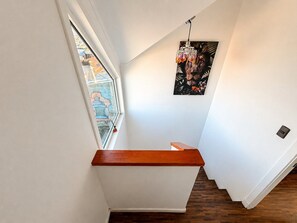 A modern staircase with a wooden handrail, a view of the outside through a window, and a wall-mounted light fixture. - Oceana Suites Punta Arenas (Punta Arenas)