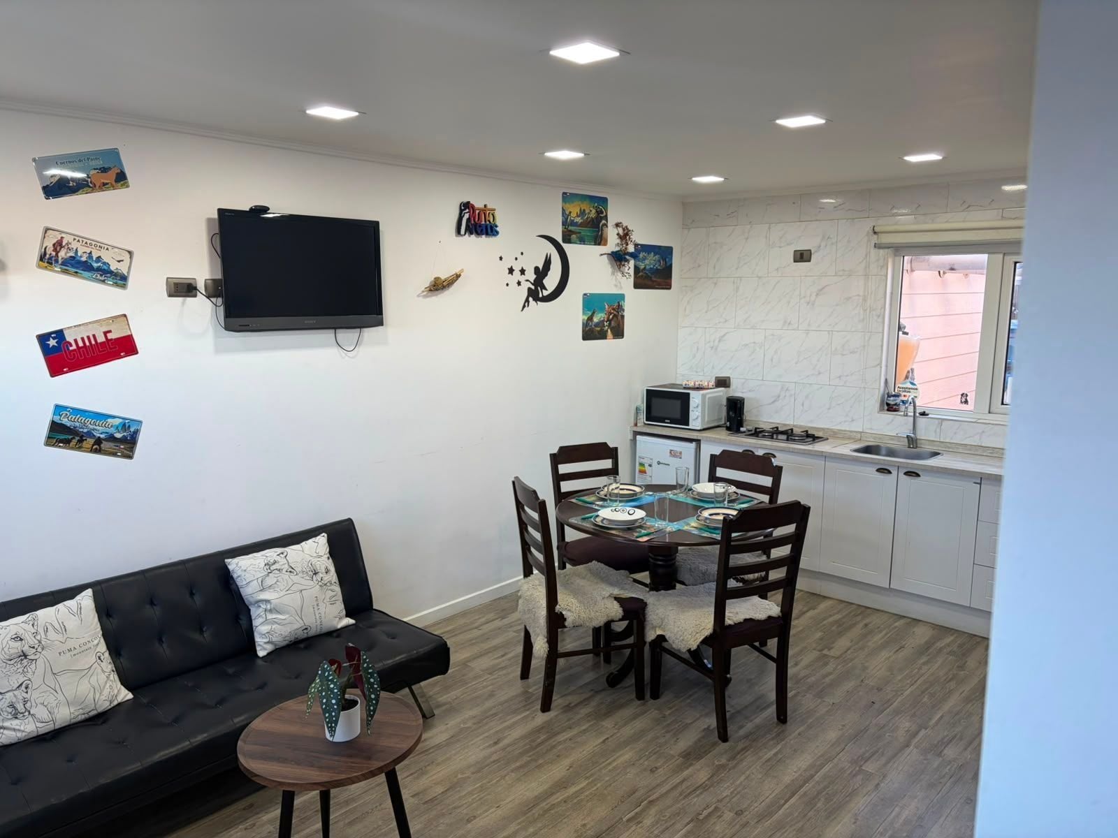 Un espacio habitable compacto con sofá, mesa de comedor, sillas, televisor y zona de cocina.