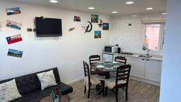 Un espacio habitable compacto con sofá, mesa de comedor, sillas, televisor y zona de cocina.
