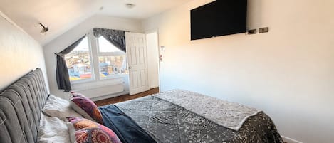 A bedroom with a bed, a window, a door, and a TV mounted on the wall.