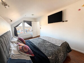 A bedroom with a bed, a window, a door, and a TV mounted on the wall.