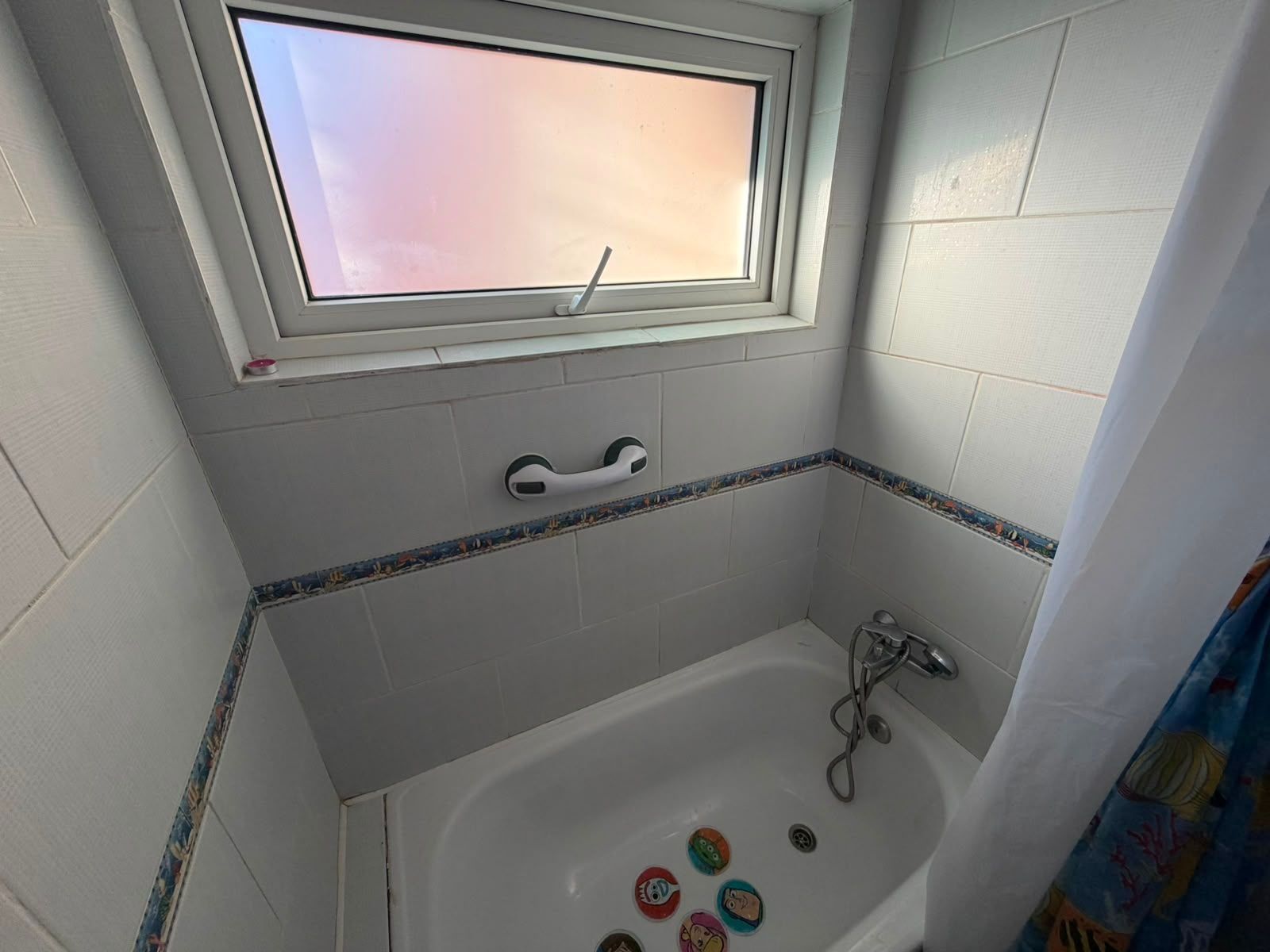 A bathroom with a bathtub, a window, and a handrail.