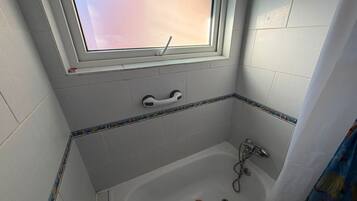 A bathroom with a bathtub, a window, and a handrail.