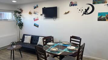 Un área de comedor con una mesa redonda para cuatro personas, un sofá y un televisor montado en la pared.