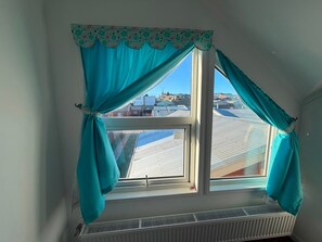 Una habitación con ventana, cortinas color turquesa y vistas a tejados.