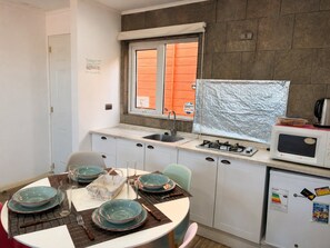 Cocina compacta con estufa a gas, microondas y pileta. Se aprecia una mesa de comedor con platos y cubiertos.