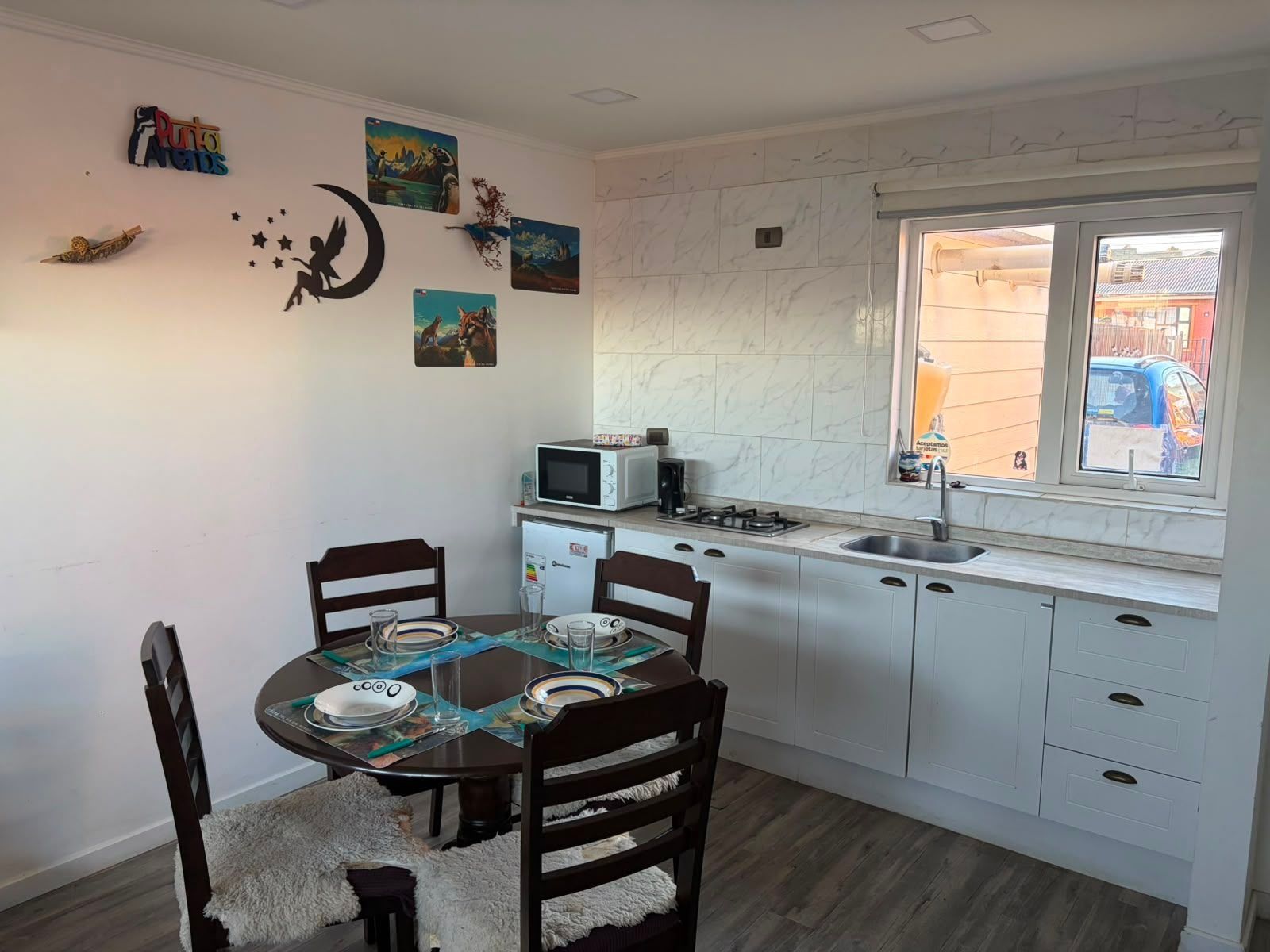A compact kitchen with white cabinets, a microwave, a sink, and a window overlooking a street.