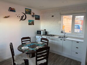 Una cocina compacta con armarios blancos, microondas, lavabo y ventana con vista a la calle.