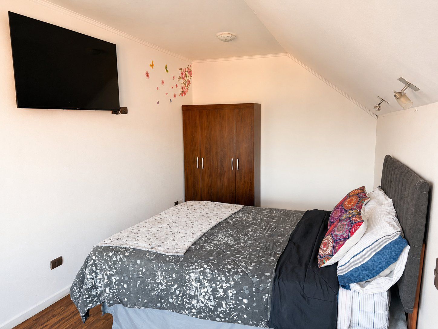 A bedroom with a bed, a wardrobe, a flat-screen TV, and a ceiling fan.