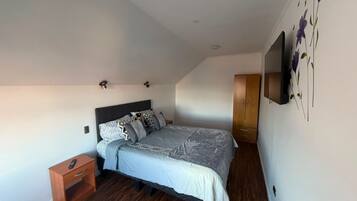 Un dormitorio con cama, mesita de noche, armario y televisor en la pared.