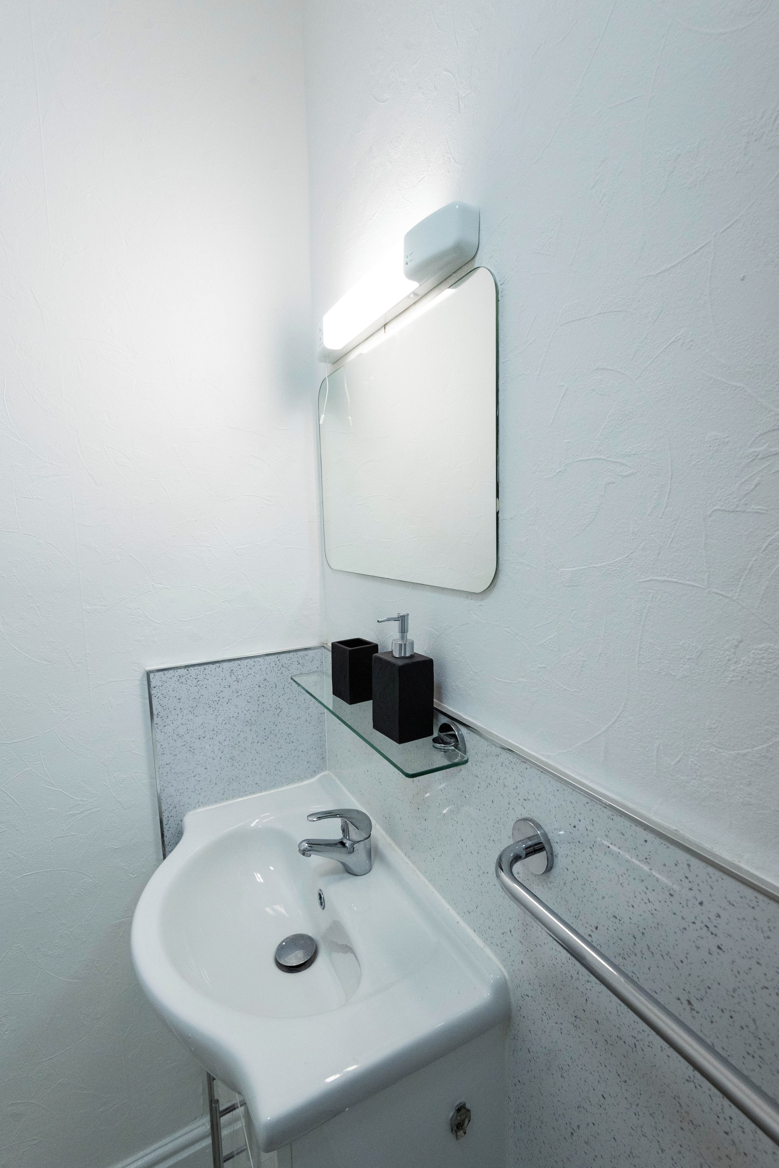 A bathroom with a white sink, a mirror, a soap dispenser, and a hand dryer.