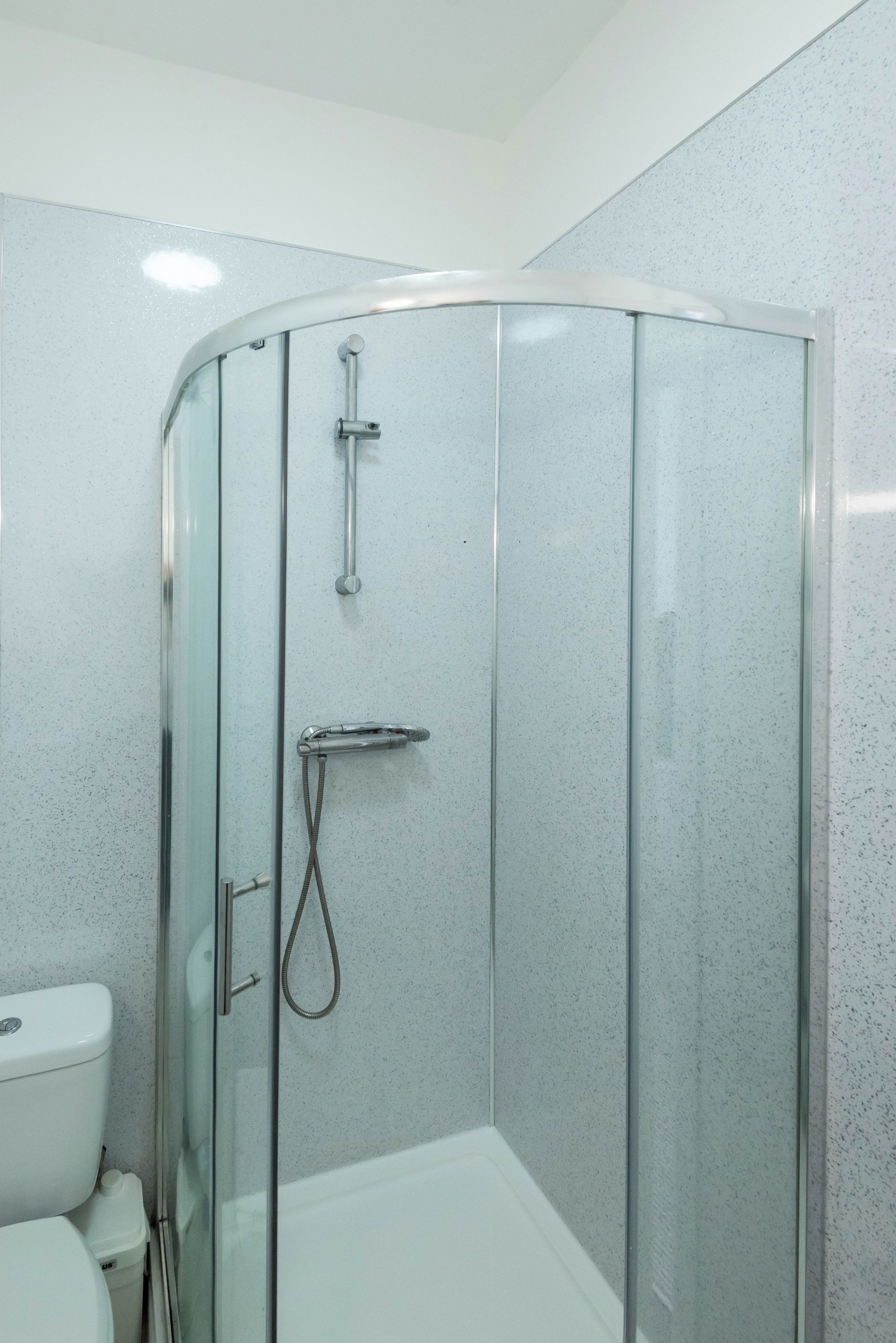 Cabina de ducha con paredes de vidrio, cabezal de ducha de mano y grifo instalado en la pared.