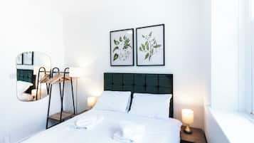 A hotel room with a bed, two bedside lamps, a mirror, a wooden side table, and two framed botanical prints on the wall.