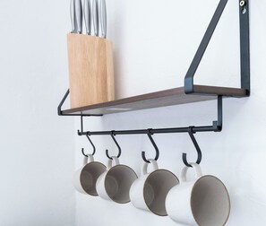 A wall-mounted shelf with a wooden block and metal hooks holding white mugs.
