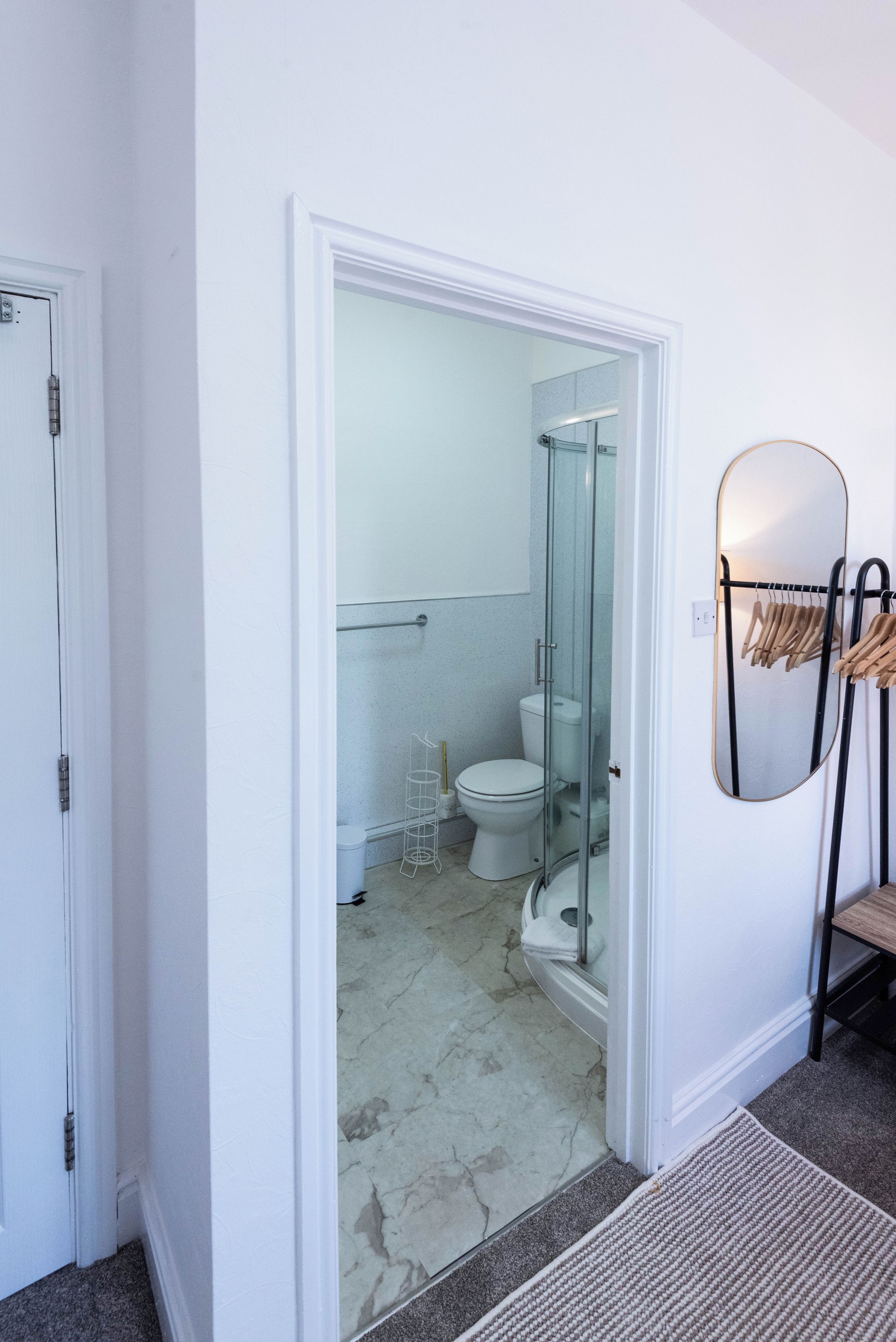 A bathroom with a glass shower enclosure, a toilet, and a towel rack with hangers.