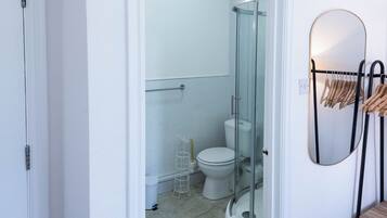 A bathroom with a glass shower enclosure, a toilet, and a towel rack with hangers.