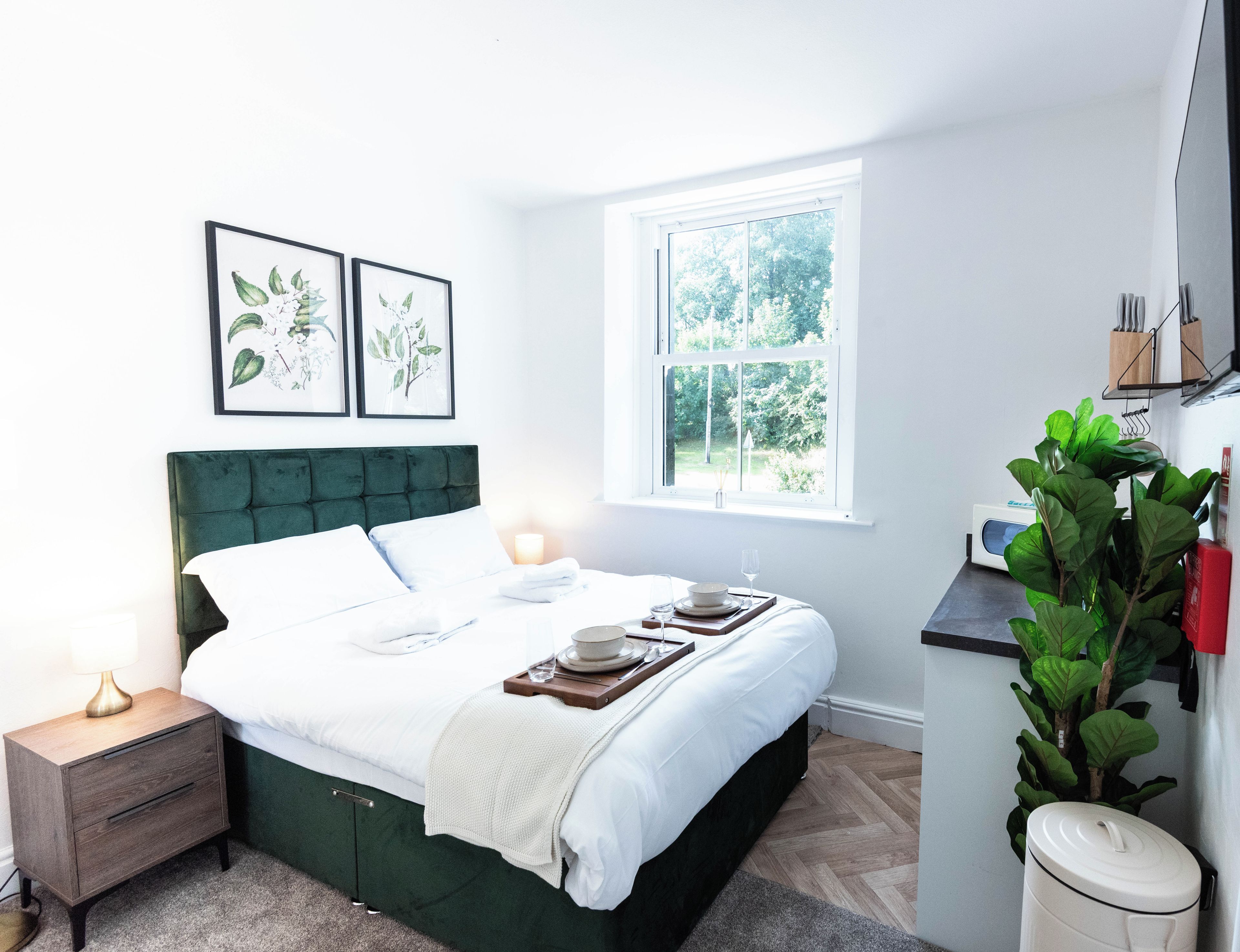 A neatly arranged bedroom with a bed, bedside table, and a window providing a view of greenery.
