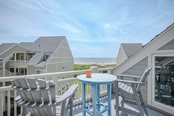 A balcony with a table and chairs overlooking a beach. - Casa De Ava: Ocean Views and Easy Beach Access (Oak Island)