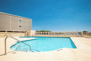 A swimming pool with a clear blue water, surrounded by lounge chairs and a building with a flat roof. - Casa De Ava: Ocean Views and Easy Beach Access (Oak Island)