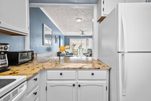 A kitchen with white cabinets, a granite countertop, a microwave, a toaster, and a refrigerator. - Casa De Ava: Ocean Views and Easy Beach Access (Oak Island)