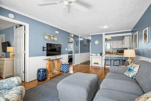 A living room with a sofa, a television, and a decorative sign on the wall. - Casa De Ava: Ocean Views and Easy Beach Access (Oak Island)