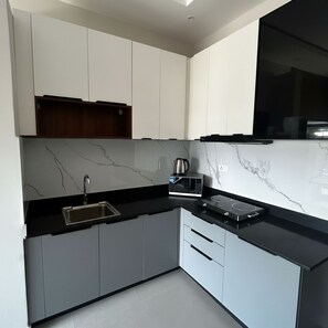 A modern kitchen with white cabinets, a black countertop, a built-in microwave, and a stove. - Urban Oasis Apartment (Serrekunda)