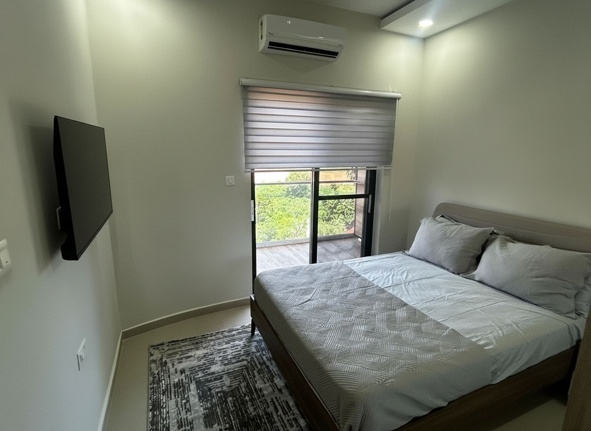 Een slaapkamer met een bed, een aan de muur bevestigde televisie, een raam met zonwering en een airconditioning.