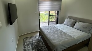 Une chambre à coucher comprenant un lit, un téléviseur fixé au mur, une fenêtre avec des stores et un appareil de climatisation.
