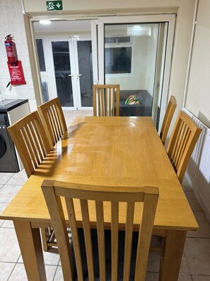 A wooden dining table with six chairs, a fire extinguisher, and a fire blanket on the wall. - Spacious 6 Bedroom Home for Families&contractors (Hornchurch)