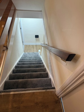 A carpeted staircase with a handrail, wooden floor, and a white wall with a power outlet. - Spacious 6 Bedroom Home for Families&contractors (Hornchurch)