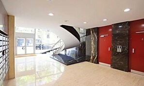 Um lobby moderno com uma escadaria sinuosa, paredes de mármore e uma porta de vidro que dá para o exterior.